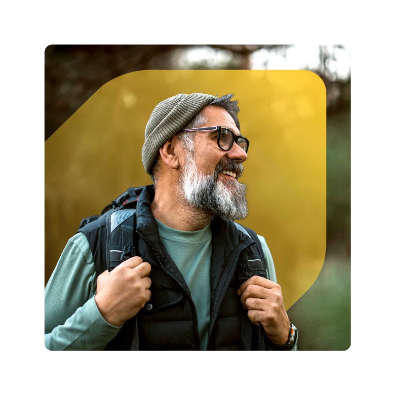 Photo of smiling older bearded man wearing hiking gear, set against EQ Bank extended jewel symbol, with natural landscape in background.