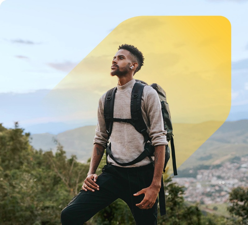 A man with a backpack stands atop a mountain, enjoying the panoramic scenery of the valleys and hills below.